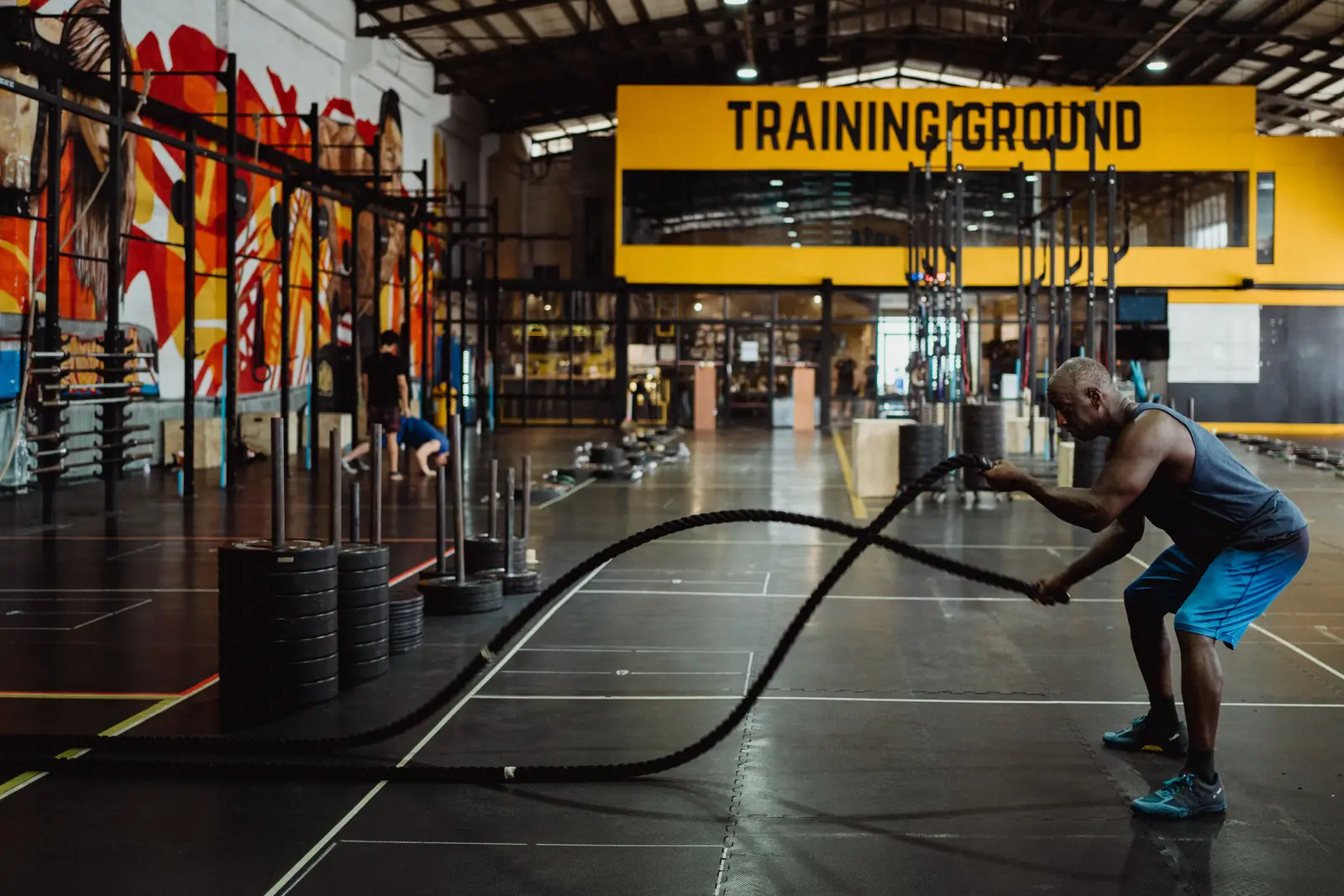 A client works the battle ropes in a big open gym.