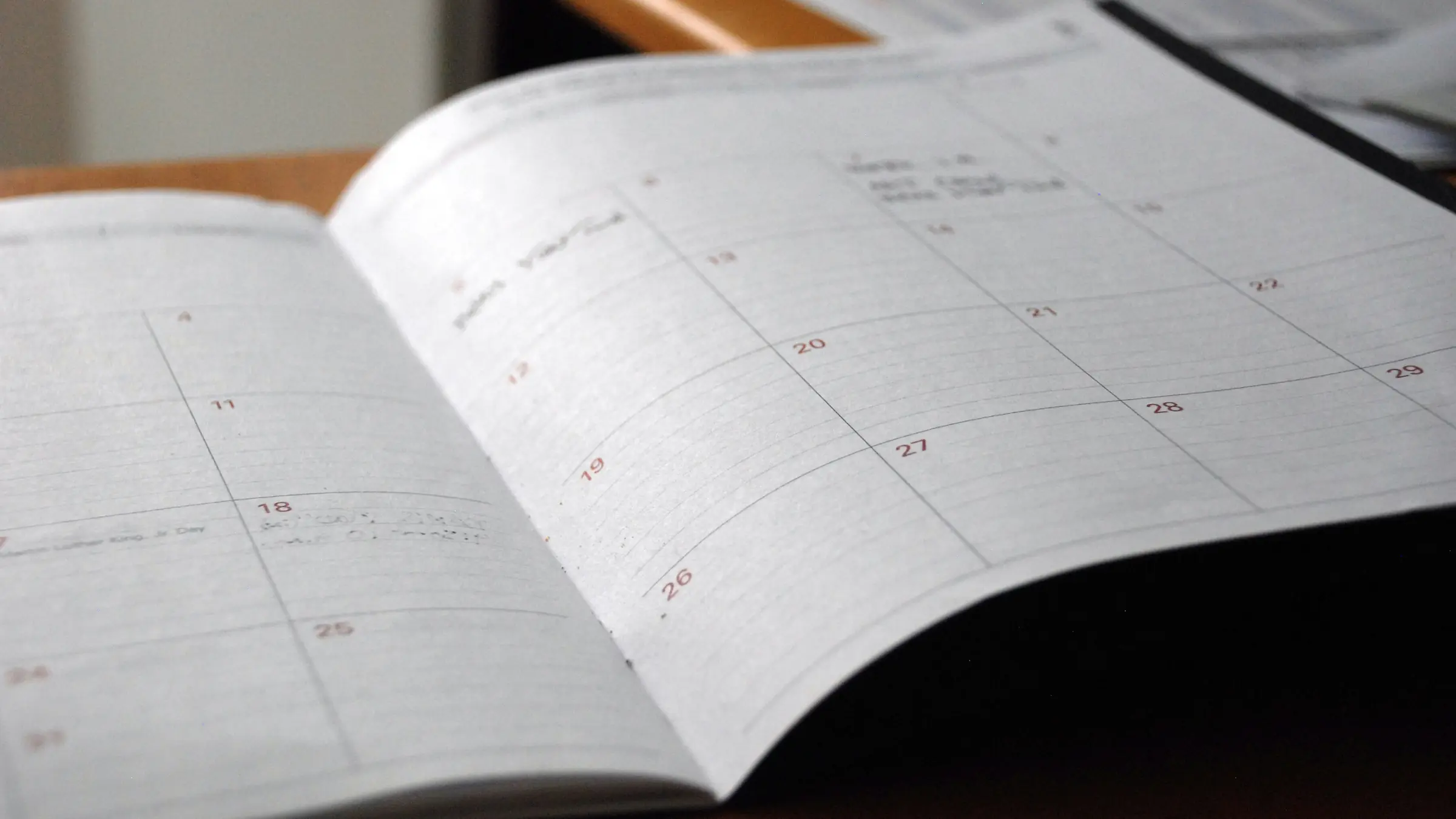 An open monthly planner on a wooden desk, a few dates filled in by hand.